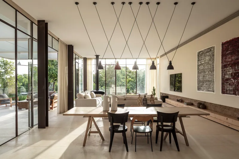 Open living and dining area with pendant lights on crossed cables and floor-to-ceiling glazing overlooking trees
