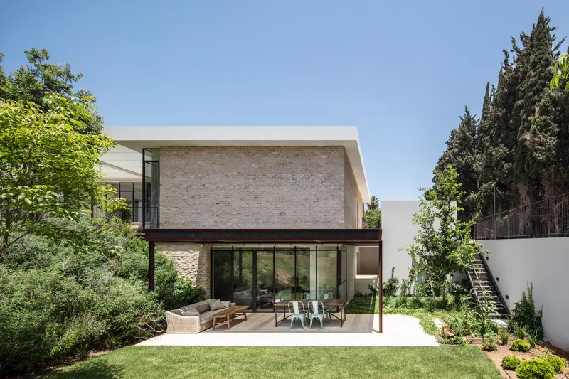 Garden view of the two-story volume with light brick cladding above a glazed terrace with outdoor furniture