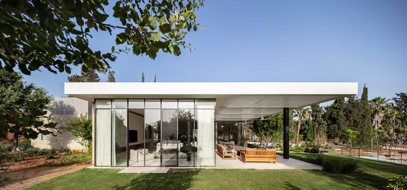 Freestanding glazed pavilion with flat roof overhang in the garden under midday sun