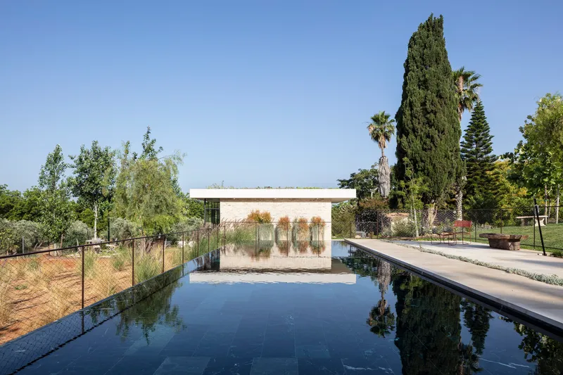 Stone pool pavilion with planted roof reflecting in the dark water under a clear summer sky