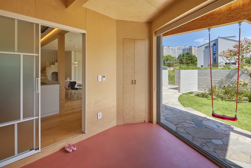 Interior threshold space with terracotta floor opening to garden with red swing hanging from tree