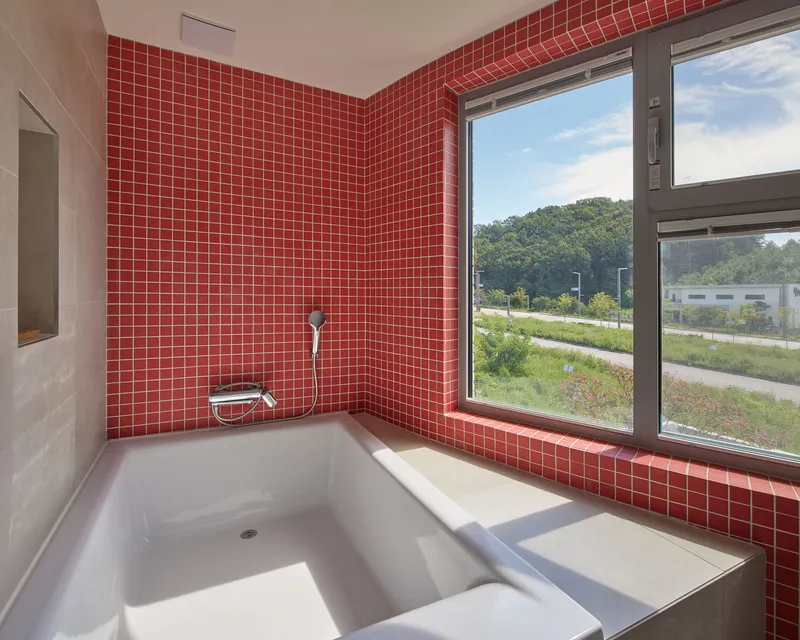 Sunken bathtub surrounded by red mosaic tile walls with a corner window overlooking green vegetation