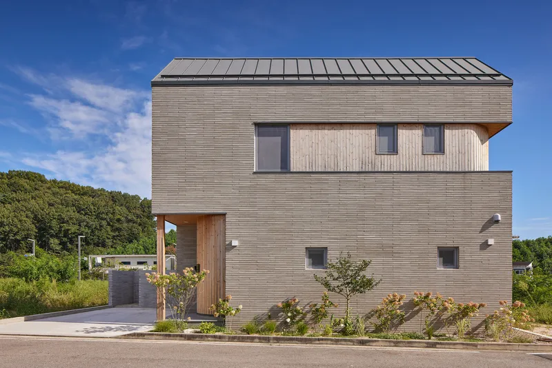Street facade clad in horizontal timber siding with punched windows and a covered entry beneath blue sky