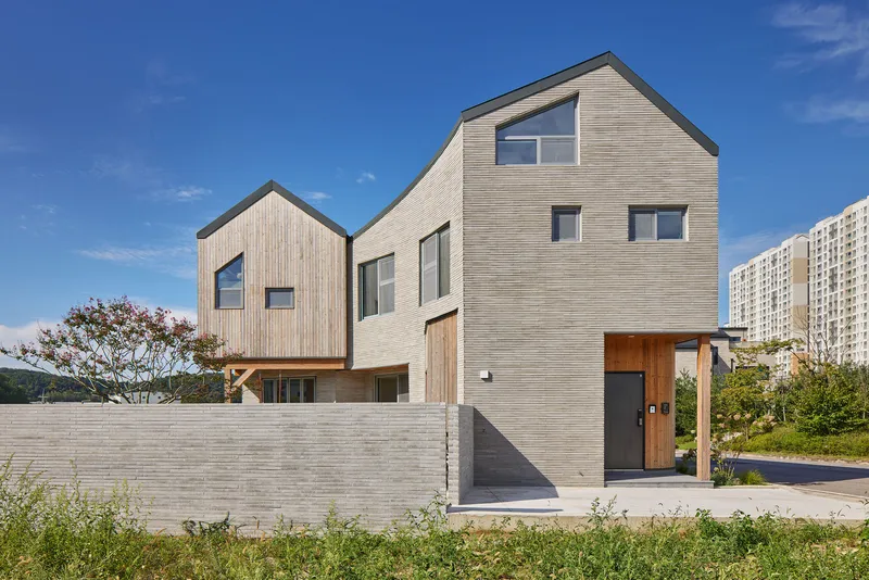 Two gabled volumes clad in horizontal wood siding with a concrete block boundary wall on a grassy lot