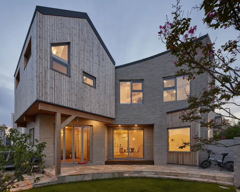 Rear courtyard showing glazed openings with warm interior light at dusk framed by flowering trees