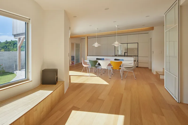 Open living and dining space with light wood flooring and pendant fixtures over a table with colorful chairs