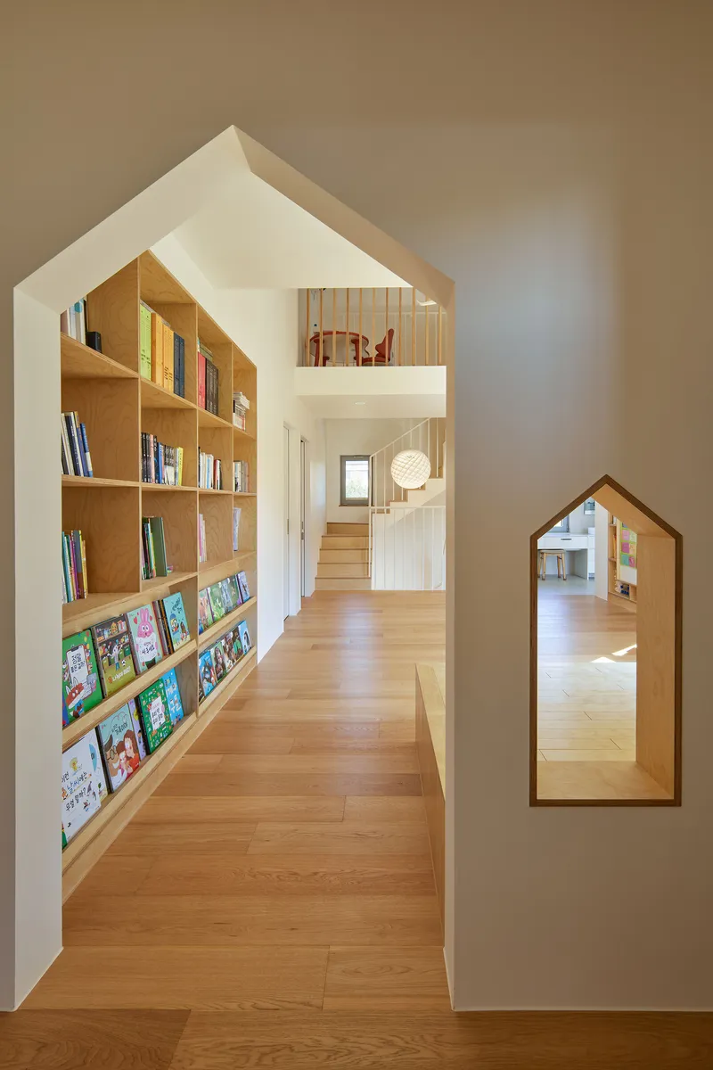 Gable-shaped passageway with built-in plywood bookshelves and a house-shaped opening to adjacent rooms