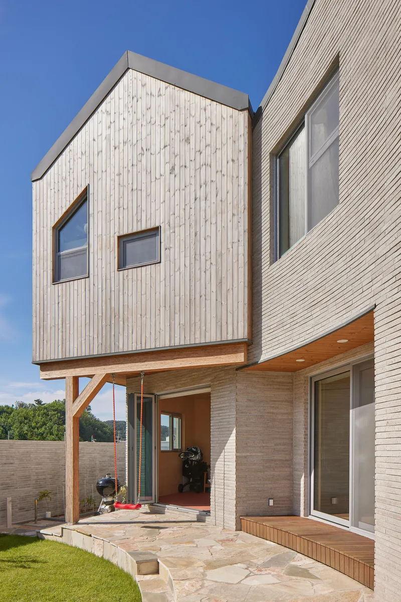 Cantilevered timber volume on exposed brackets above a stone terrace and lawn under blue sky