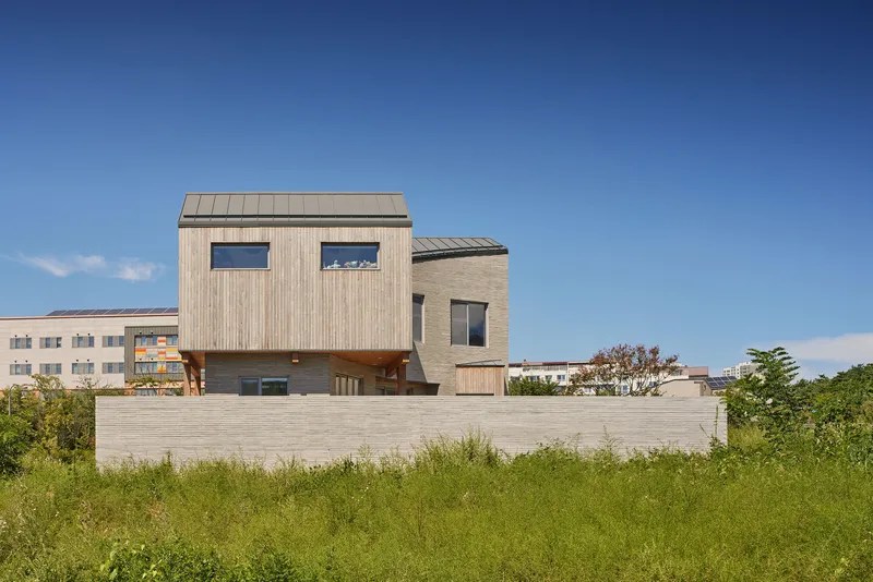 Rear elevation showing two timber-clad volumes raised above a horizontal plinth wall in a grassy field