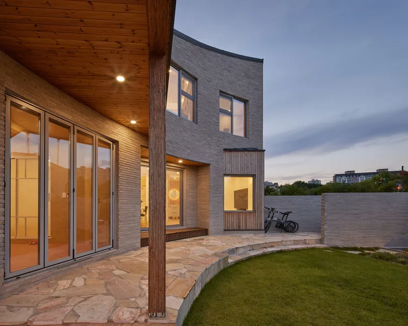 Rear courtyard with stone paving and timber column at dusk beneath a wood-lined soffit