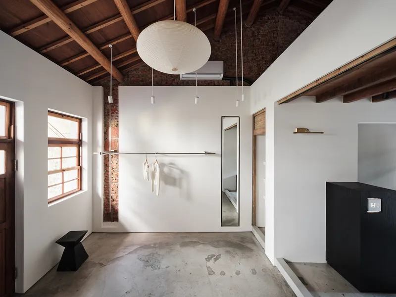 Retail room with concrete floor, exposed brick column, and wall-mounted clothing rail casting soft shadows