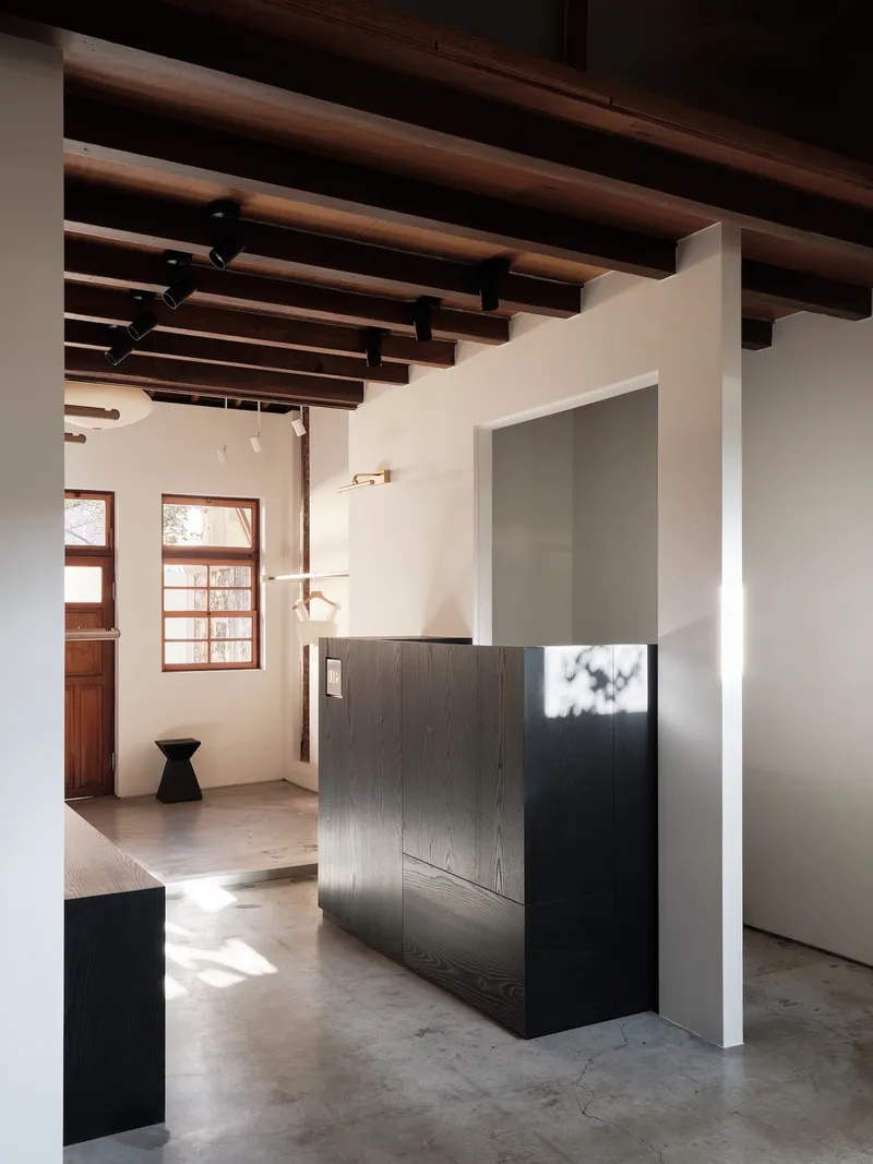 Black display cabinet beneath exposed timber ceiling joists with pendant lights and wooden door beyond