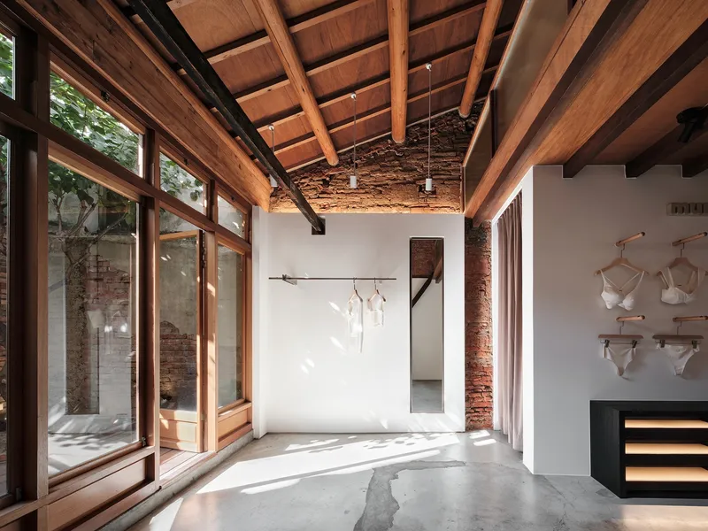 Interior room with timber-framed glazing overlooking courtyard, concrete floor, and dappled afternoon light