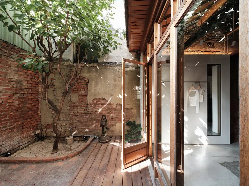 Interior courtyard with timber decking, reclaimed brick walls and young tree casting dappled shadows
