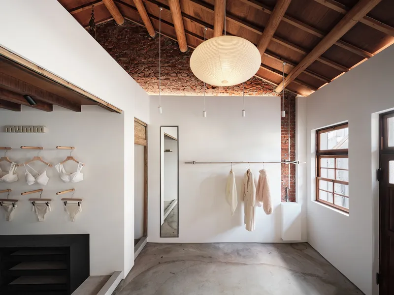 Interior retail space with exposed timber ceiling, pendant light, and concrete floor receiving morning sunlight