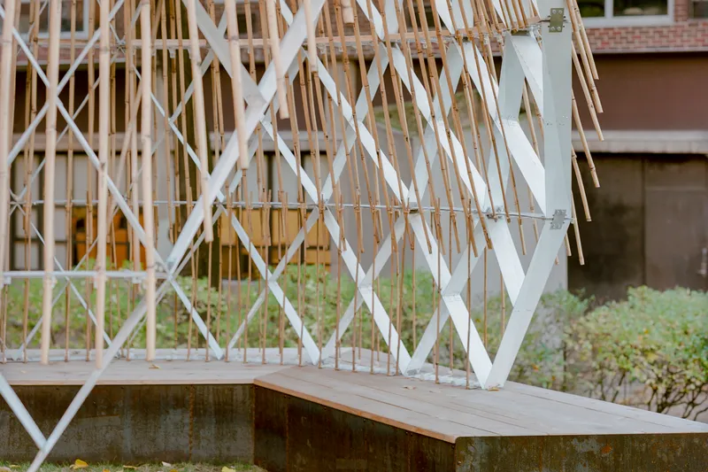 Detail of the timber lattice base where white diagonal members meet the weathered concrete plinth and timber bench