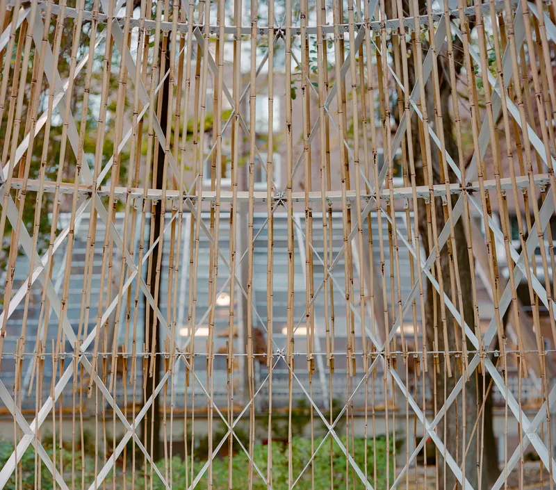 Lattice facade with vertical bamboo slats and diagonal white bracing against foliage backdrop
