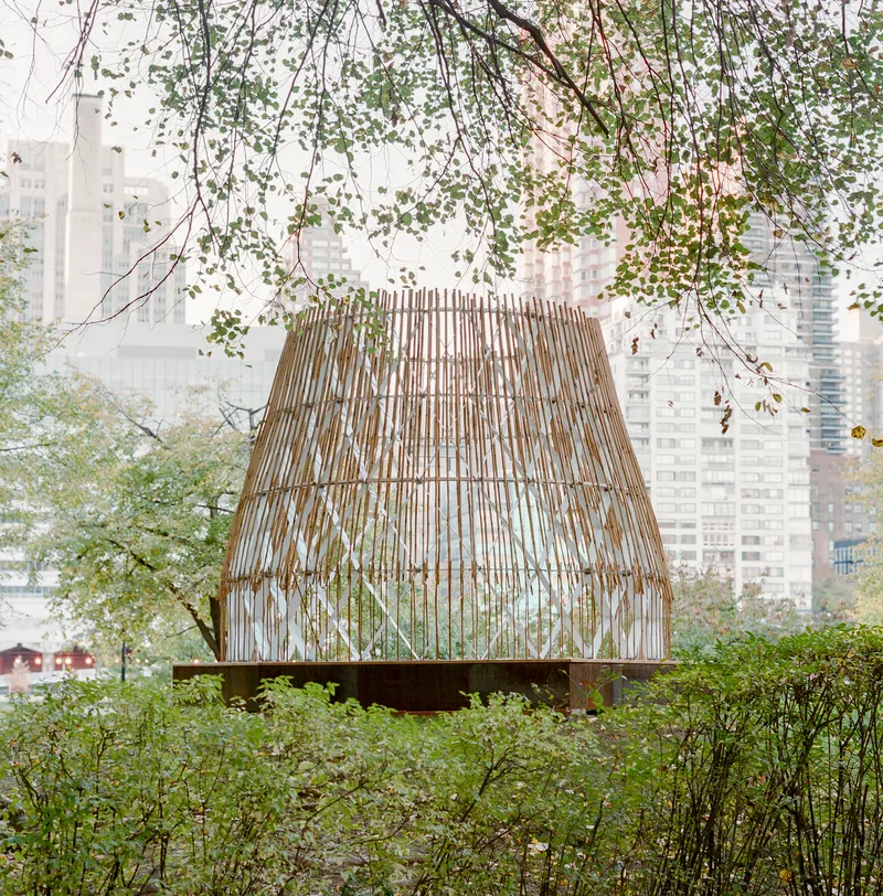 View of the slatted pavilion through hanging willow branches in morning mist