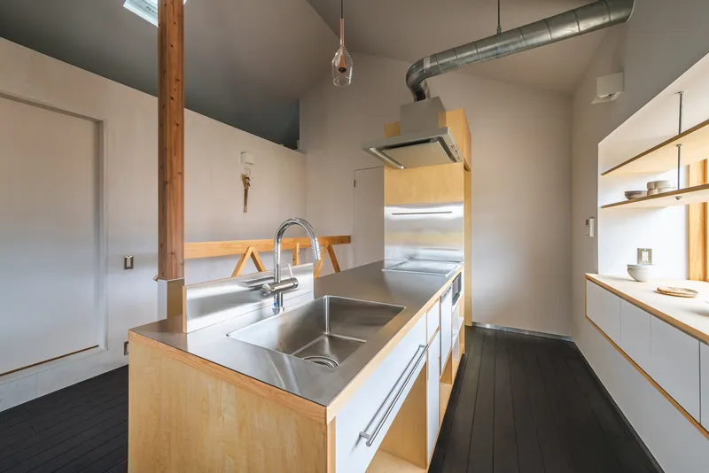 Kitchen island with stainless steel sink beneath exposed ductwork and a recessed ceiling vent