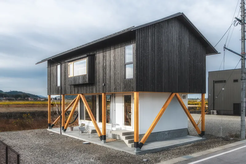 Exterior view showing charred timber cladding above white stucco with diagonal timber bracing at ground level