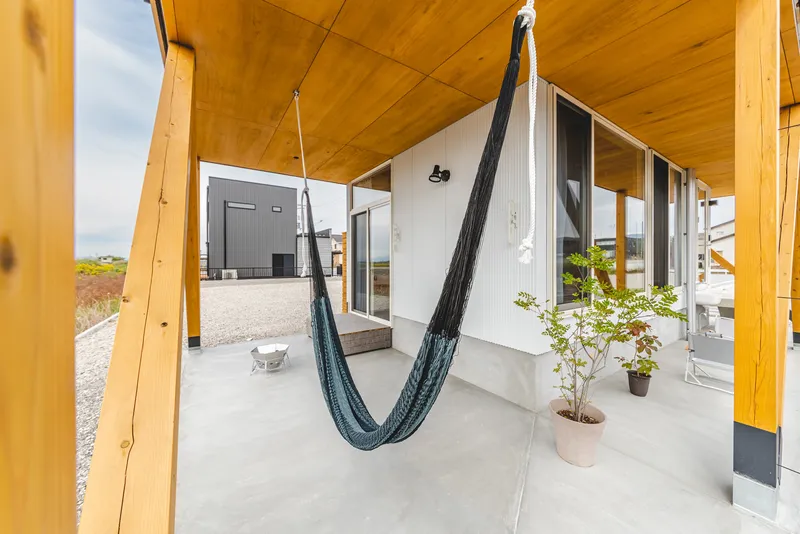 Ground-level covered terrace with yellow timber columns, concrete slab, hammock, and potted plants