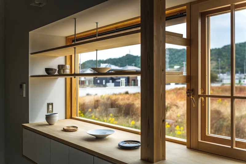 Kitchen counter and open shelving beside glazed doors overlooking autumn grasses and mountains