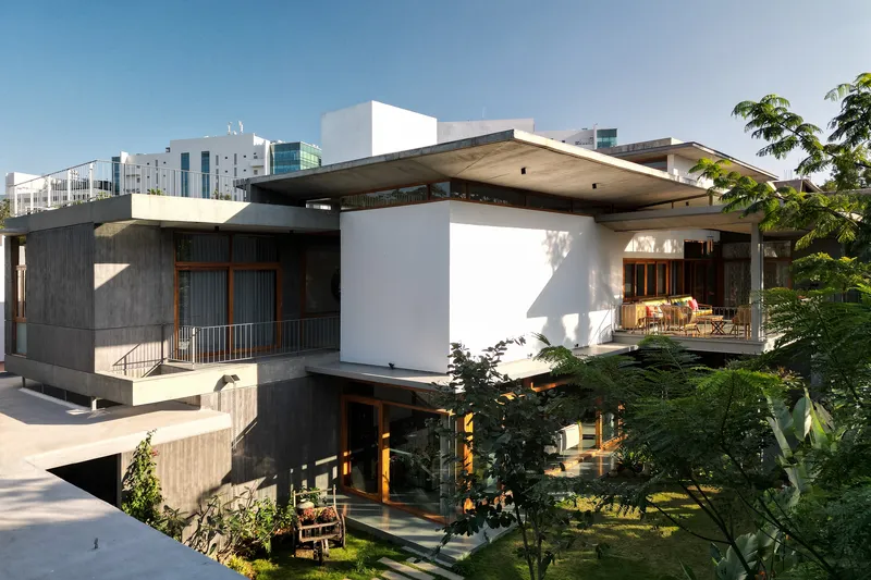 Exterior view of cantilevered concrete roof planes sheltering white volumes and a planted garden below