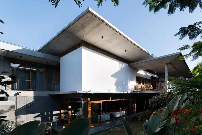 Elevated white volume supported by timber columns above a transparent ground floor in afternoon light