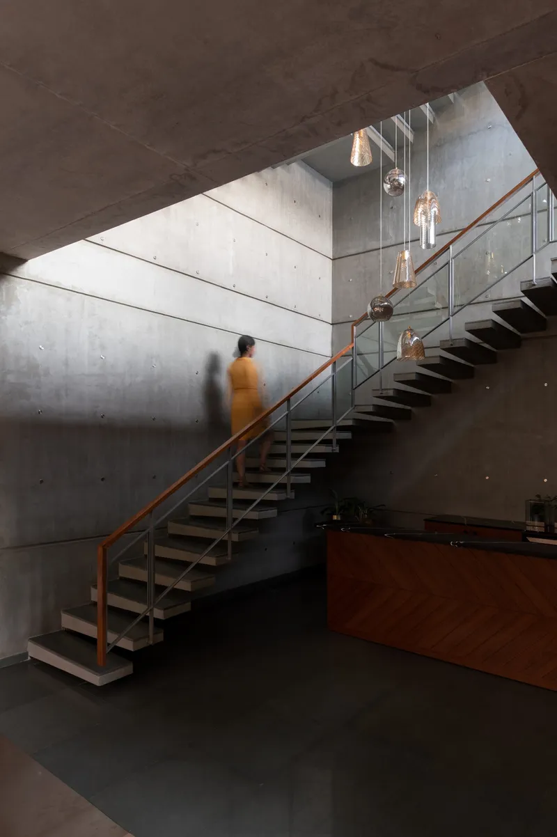Steel and timber staircase with glass balustrade ascending concrete walls toward a skylight with pendant fixtures