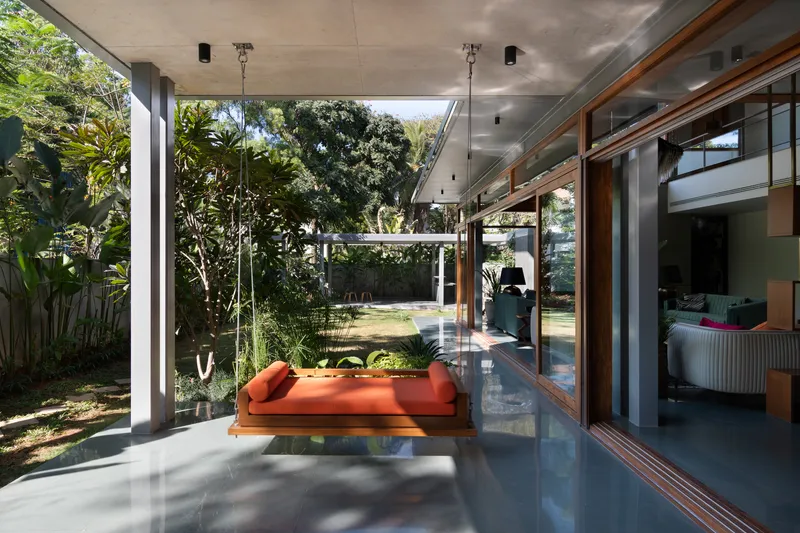 Covered terrace with suspended daybed overlooking garden through floor-to-ceiling sliding glass doors