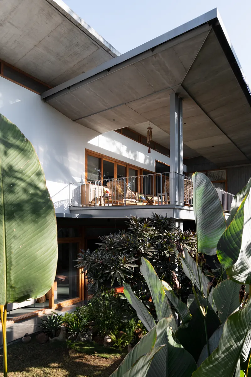 Elevated terrace with timber framing and steel column seen through lush banana and tropical planting
