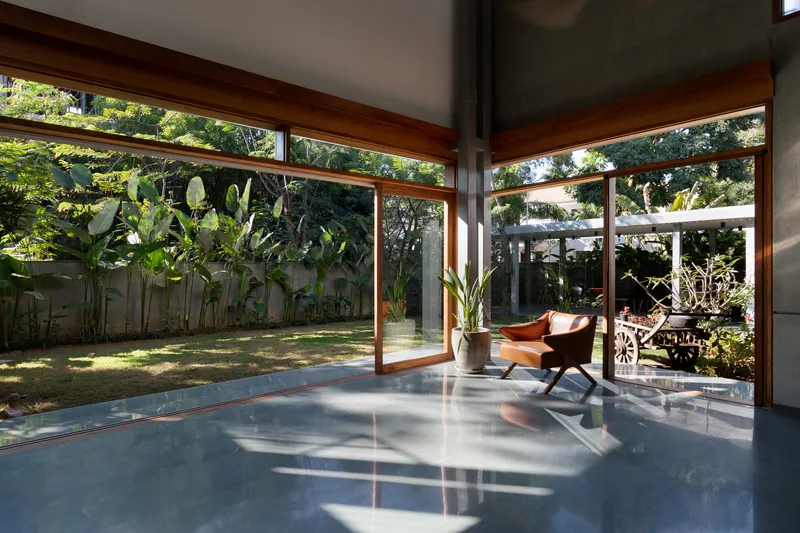 Glass-walled interior space with timber frames opening onto a grassed courtyard with banana plants