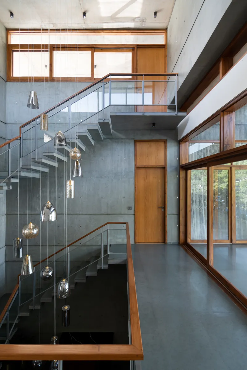 Double-height stairwell with concrete walls, glass balustrade, and suspended pendant lights over the void