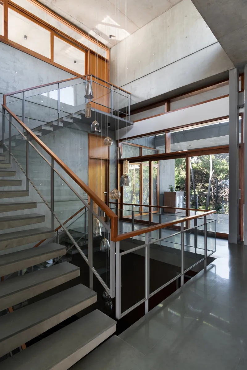 Central staircase with glass and timber railings linking split levels beneath exposed concrete ceilings