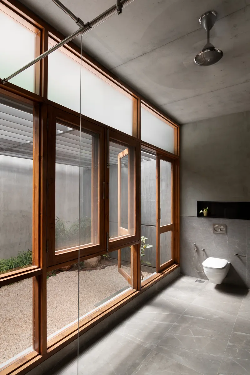 Bathroom with exposed concrete ceiling and timber-framed glazing opening to a small gravel courtyard