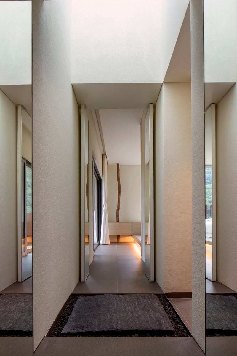 Corridor with slender recessed columns and angled wood-paneled walls leading to softly lit interior spaces