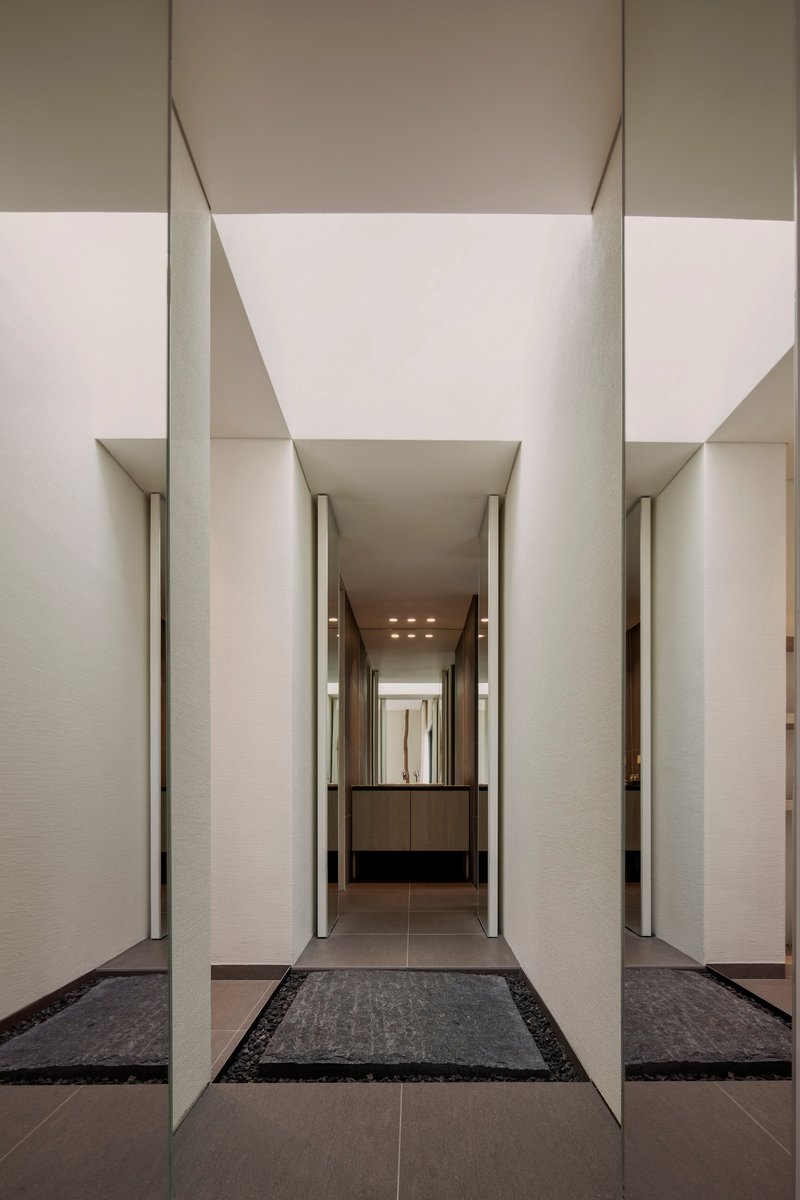 Recessed entry corridor with pale stone walls and dark floor tiles under linear ceiling beams