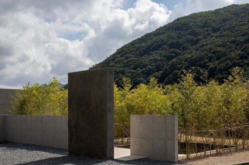 Concrete wall and monolithic tower with young bamboo grove backed by densely forested hillside