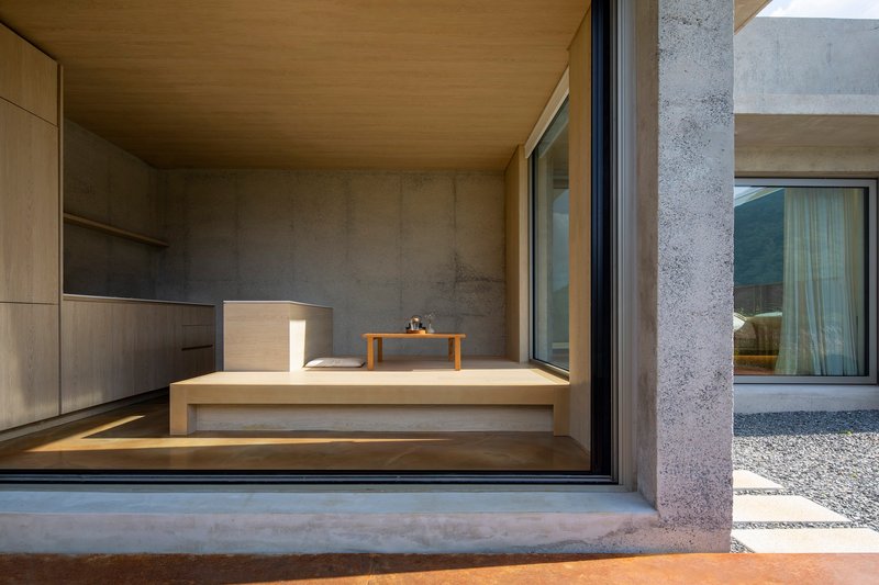 View through sliding glass doors into a timber lined room with concrete walls and gravel courtyard