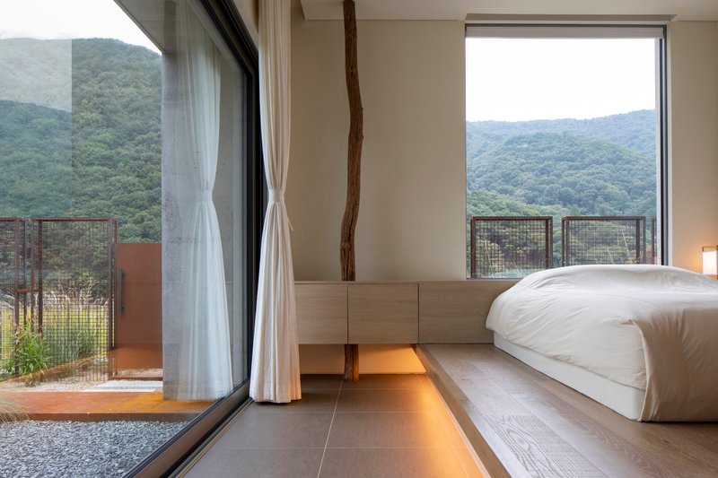 Bedroom interior with raised timber platform bed and floor to ceiling window overlooking forested mountains