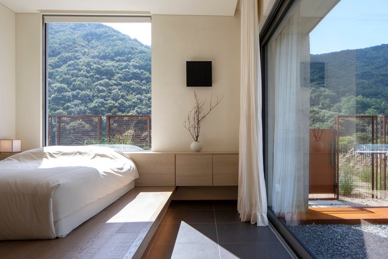 Bedroom corner with low platform bed and glass doors opening to a gravel courtyard in morning light