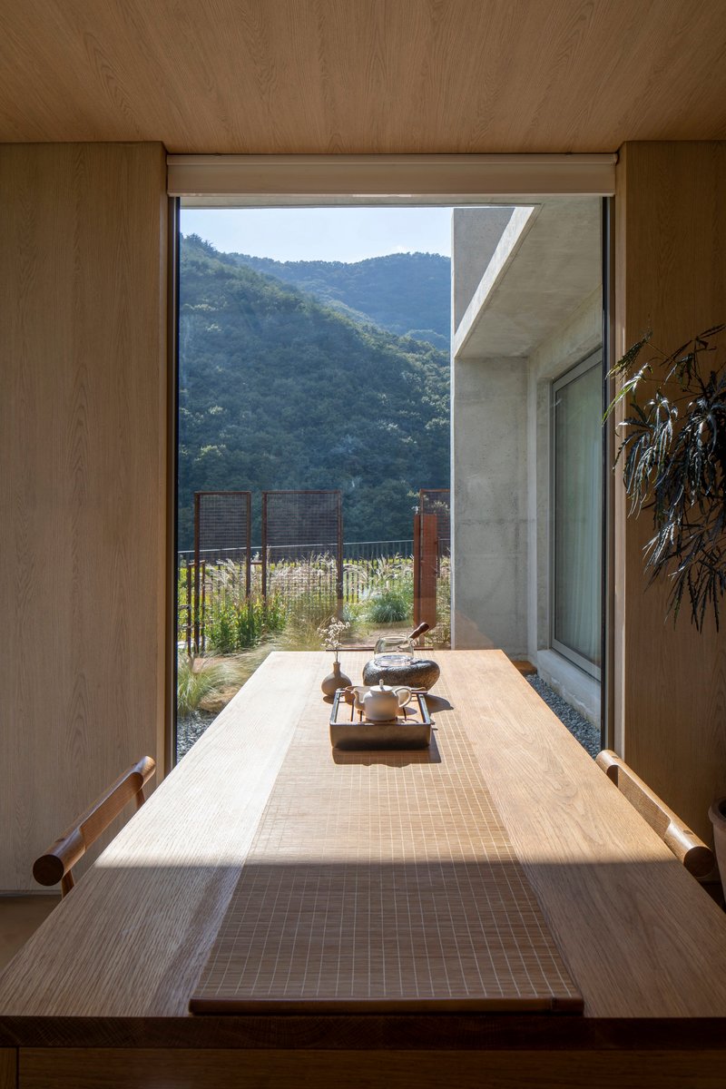 View through a timber-framed opening toward a planted courtyard with hills in the distance