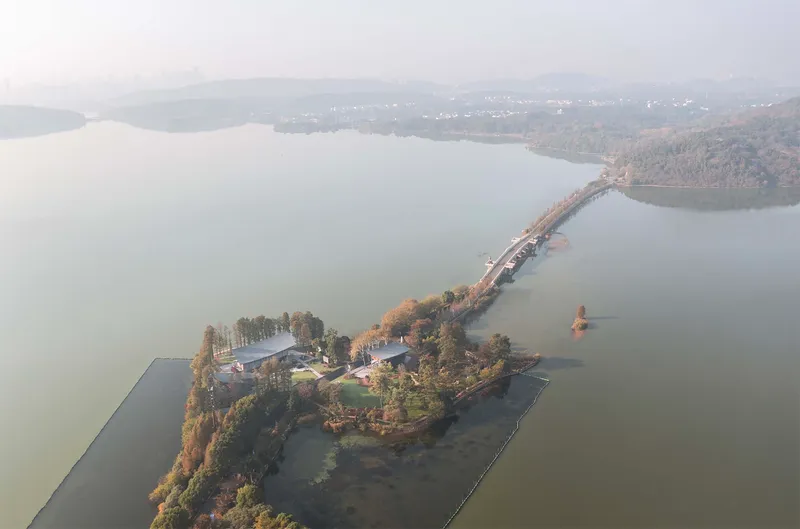 Aerial view of lakeside peninsula with buildings connected by causeway through misty water