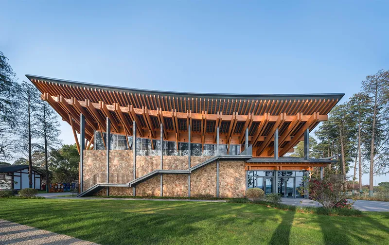 Timber-framed pavilion with exposed rafters and stone base walls on a grassy lawn at dusk