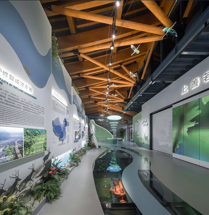 Interior exhibition hall with exposed timber roof beams, curved water feature, and suspended bird sculptures