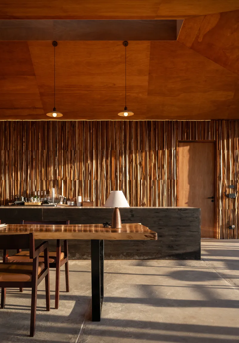 Kitchen island with dark stone base and timber dining table under warm pendant lights and geometric wood ceiling