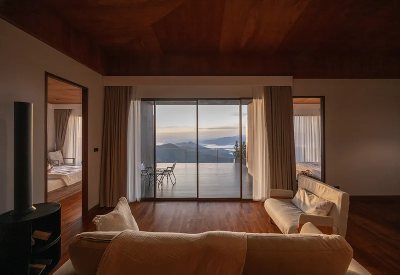 Living room with plywood ceiling and floor-to-ceiling glazing framing a mountain vista at twilight