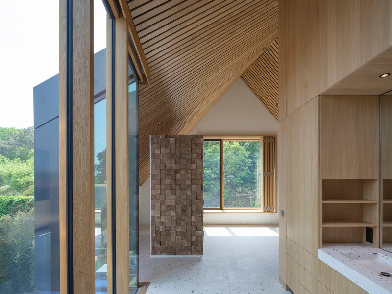 Interior with diagonal timber-slatted ceiling and textured block wall beneath the pitched roof