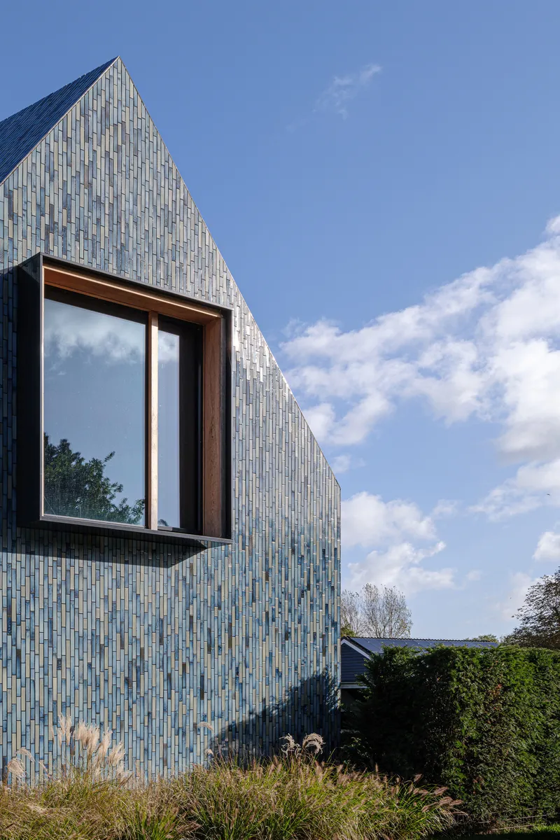 Projecting timber-framed window box set within the glazed tile facade under scattered clouds