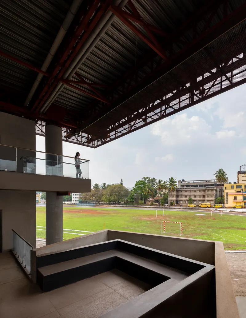 Covered terrace with concrete bleacher seating overlooking the football pitch under an exposed truss ceiling